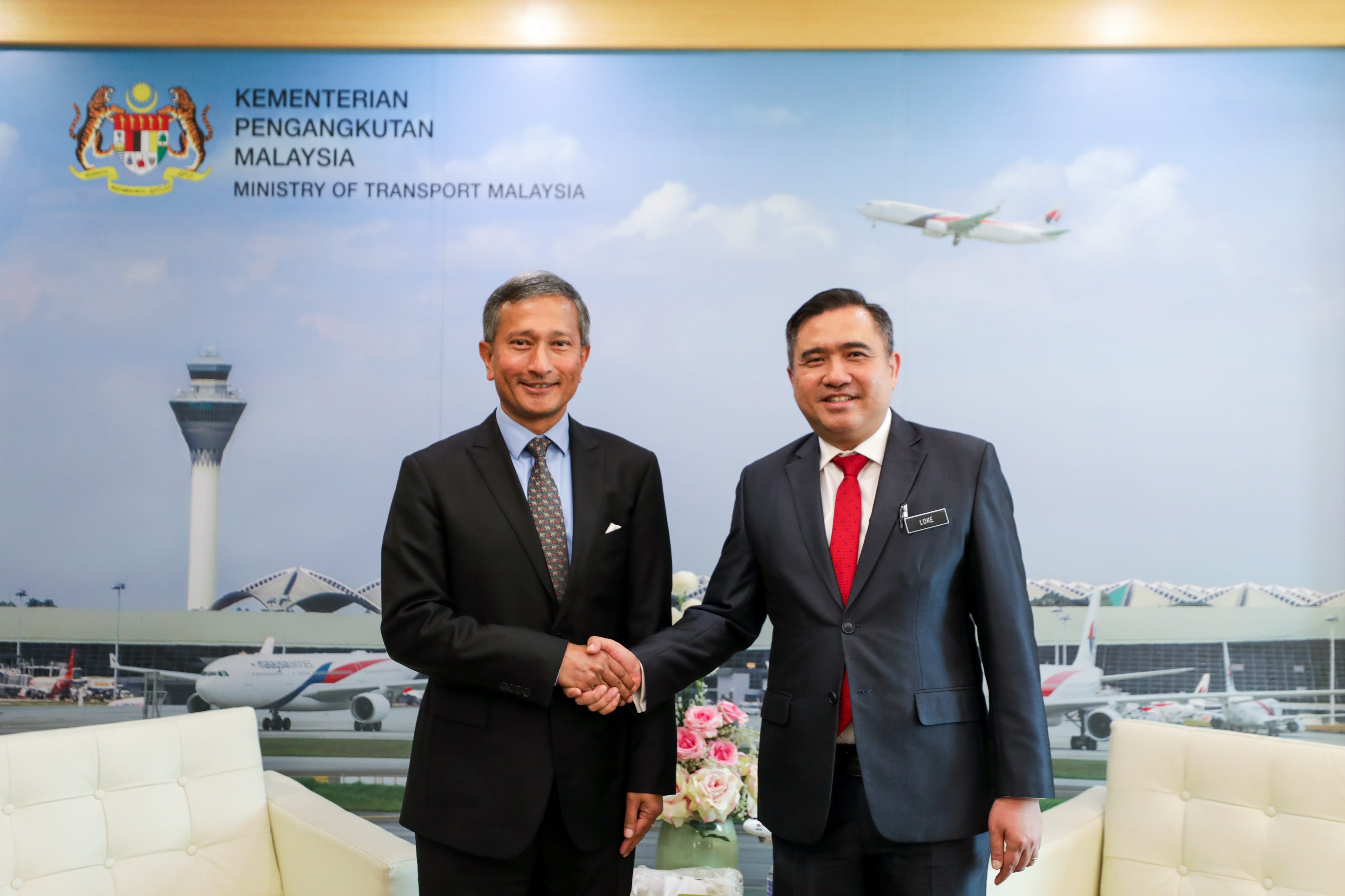 Two men in suits shaking hands in front of a Ministry of Transport Malaysia backdrop.
